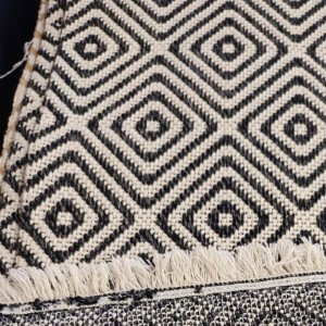 Woven rug with black parallel geometric patterns and white fringe for boho summer decor.